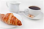 Croissant and a cup of coffee on white plates with sugar and milk against a white background