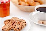 Cookies and a cup of coffee on white plates with sugar croissants and milk and a pot of jam against a white background