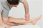 Serious osteopath massaging the shin bone of a patient in a room