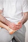 Podiatrist manipulating the foot of a woman while holding it on his thigh indoors