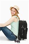 Smiling woman sitting against a suitcase against white background