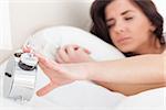 Brunette woman trying to turn off her alarm clock in her bedroom