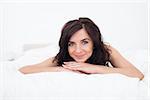 Brunette woman lying on her white duvet in her bedroom