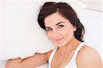 Brunette woman lying while placing her hand under a pillow in her bedroom