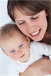 Cheerful mother holding her cute baby against a grey background