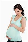 Young pregnant woman looking at her belly against white background