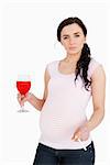 Pregnant young woman holding alcoholic drink and cigarette against white background