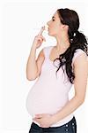 Young pregnant woman smoking against white background