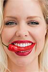 Close-up of a cheerful blonde woman placing a chili between her teeth