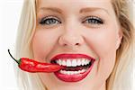 Happy blonde woman biting a red chili pepper against a white background