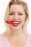 Happy blonde woman biting a chili against a white background