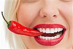 Smiling woman holding a chili with her teeth against a white background