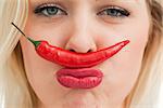 Cheerful woman placing a chili between her nose and her mouth against a white background