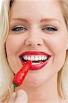 Happy blonde woman eating a chili against a white background