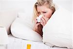 Blonde woman sneezing in her bed