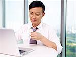 young asian businessman looking at computer and drinking coffee in office.