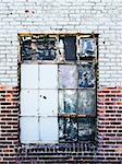 A boarded up window with broken panes is common with old brick warehouses in areas of urban decay.