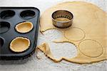 Circles being cut from fresh pastry to and filling a bun tin to make jam tarts