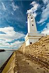 The Ciboure lighthouse, at the channel entry, under a vibrant blue sky full of fluffy clouds.