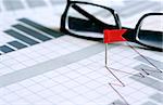 Business concept. Red flag thumbtack near spectacles on paper background with business chart