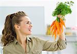 Happy young housewife holding carrots in kitchen