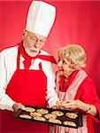 Professional baker shares a tray of fresh chocolate chip cookies with a sweet senior housewife.