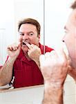 Man flossing his teeth in the bathroom mirror.