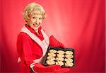 Sweet adorable grandmother holding a pan of freshly baked chocolate chip cookies.   Photographed over red background with room for text.