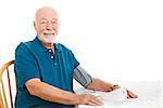 Senior man taking his blood pressure at home on the kitchen table.  White background.