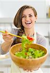 Happy young housewife giving spoon with vegetable salad