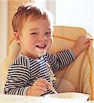 Two year old boy smiles to the camera eating porridge.