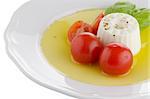 Fresh salad with goat cheese, tomato and basil pesto on a white plate.