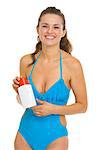 Smiling young woman in swimsuit holding sun screen creme