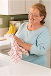 Smiling Senior Adult Woman Drying Bowl At Sink in Kitchen.