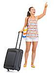 Smiling young tourist woman with wheel bag pointing on copy space