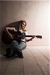 Young Woman Sitting on the Floor Playing Guitar in Studio