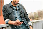 Close-up of young man texting on an iPhone in an urban setting.