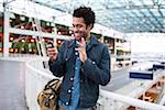 Smiling Man Waving at Cell Phone Camera during Video Chat at the Airport