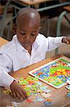 Young African schoolboy playing with a puzzle in a classroom