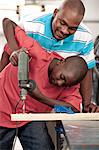 African Father and son using a drill in a workshop