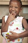 Young African child licks dough off of her finger while smiling