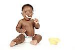 An infant sitting in front of a white background, eating.