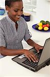Young African woman working on a laptop in the kitchen, smiling