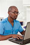 Young African man working on a laptop in the kitchen, smiling