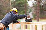 Carpenter using a nail gun to frame house