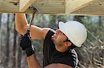 Hispanic carpenter nailing pressure treated deck joist with hammer