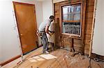 Hispanic carpenter using reciprocating saw to remove window and cut access doorway