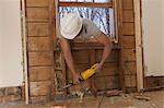 Hispanic carpenter using reciprocating saw to cut wall frame through window access