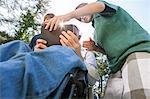 Man with spinal cord injury in wheelchair with his sons reading a tablet