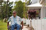 Man with spinal cord injury in a wheelchair on a suburb walk with homes